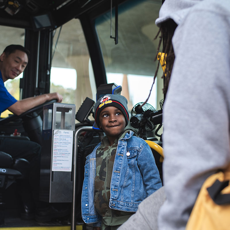 A child boards a bus with their father in the foreground and the driver watching.